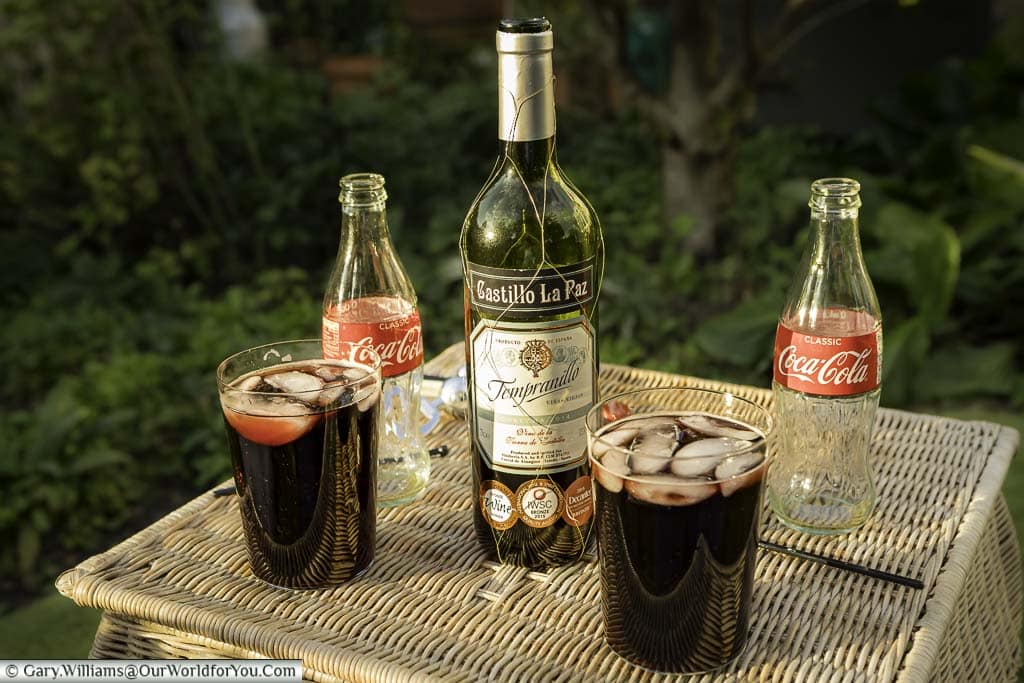 Two large straight glasses of homemade Calimocho on a wicker table in our garden in Kent, Egland