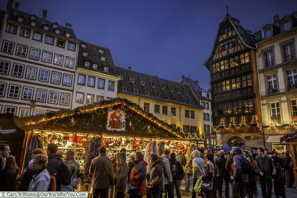 Crowds in front of strasbourg's christmas markets in the place de la cathédrale at dusk.