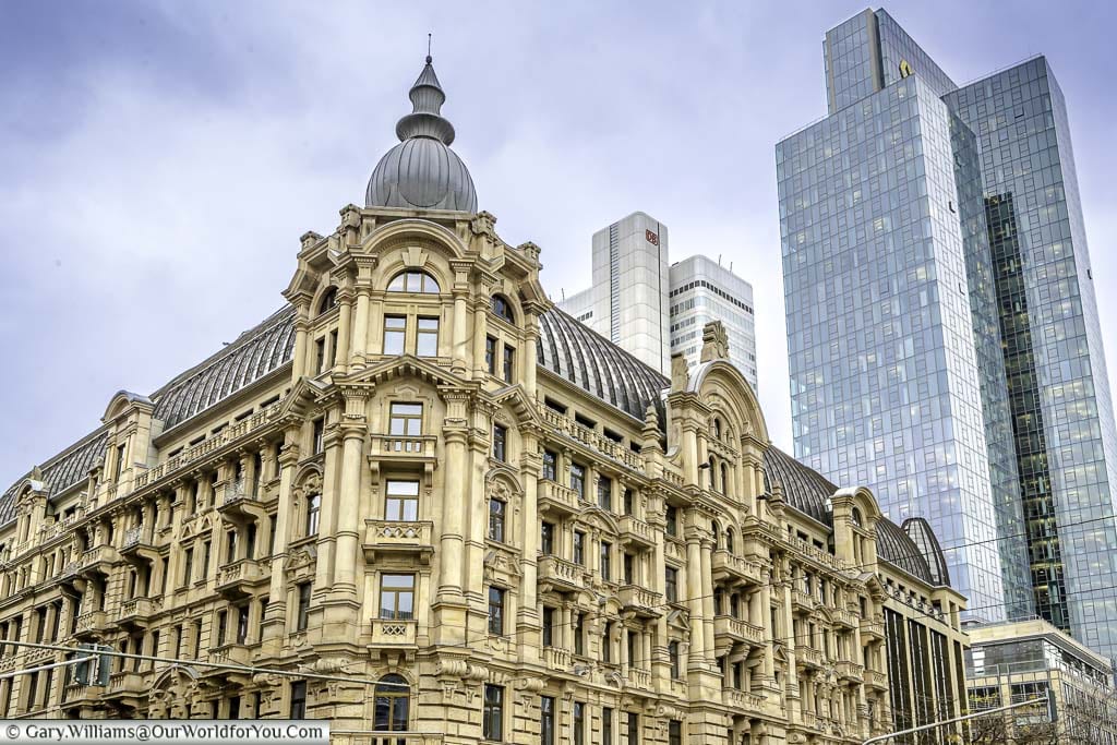 A yellow stone neoclassical building with a leaded roof in front of the glass skyscrapers of the modern Frankfurt.
