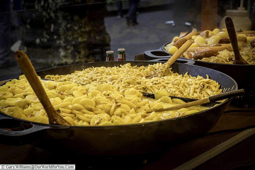 A large cast-iron open dish of Knepfle or Spaetzle, alongside another dish of Choucroute Garnie, on a Christmas market stall.