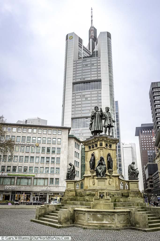 The Gutenberg Memorial in Frankfurt in front of a skyscraper. The memorial is to Johannes Gutenberg, credited as the inventor of the modern printing press.