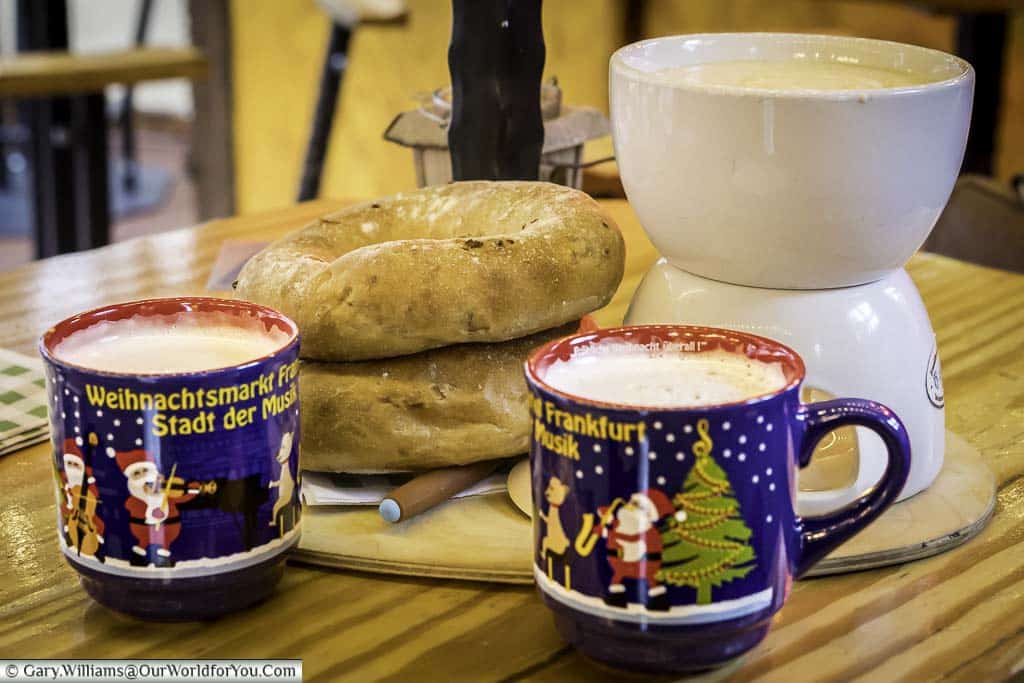 Two mugs of gluhwein in front of a fondue served with two rustic bread rolls served up on a Christmas market stall in Römerberg.