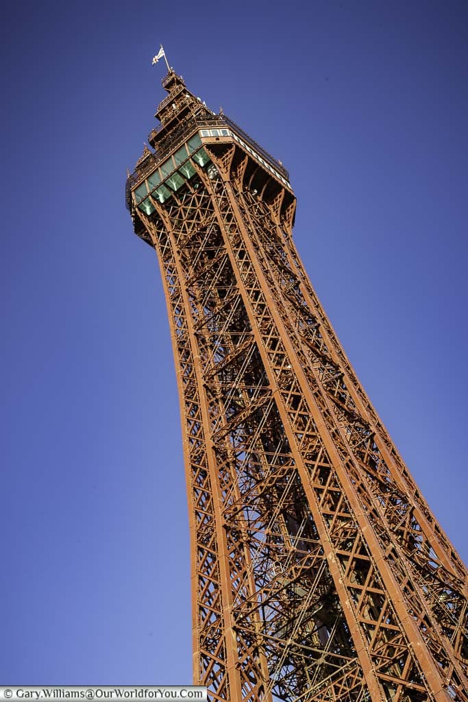 Looking up at the red ironwork of Blackpool Tower to the observation tower against a deep blue, cloudless, sky.