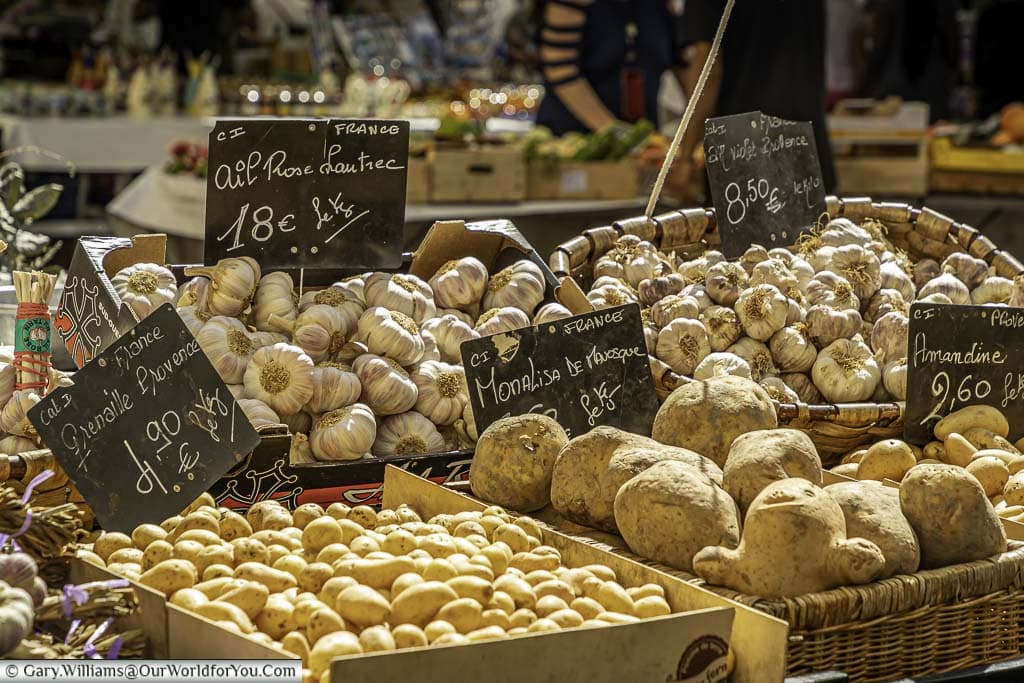 A stalling Nice, France, displaying varieties of potatoes and a selection of fresh garlic.
