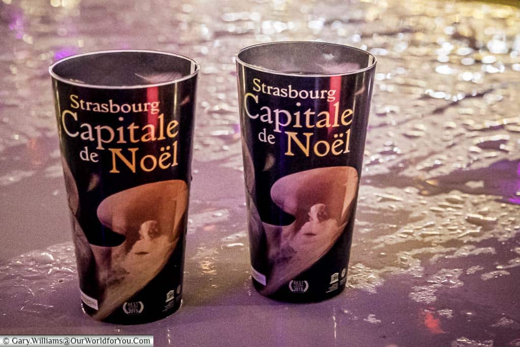 Two plastic beakers of vin chaud on the top of a wet tabletop at one of the Christmas Markets. The cups are decorated with angels and labelled with the cities Christmas tag - Strasbourg, Capitale de Noel.