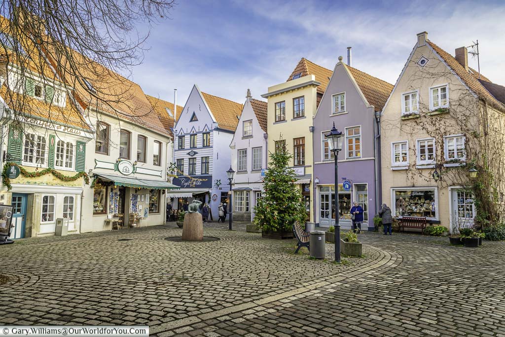 A Christmas tree in a quaint cobbled square, lined with tall thin pastel coloured historic buildings on two sides.