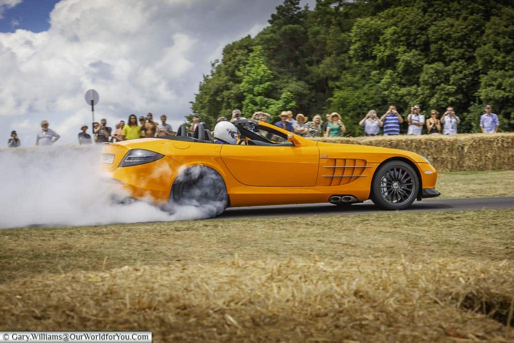 lewis hamilton waving performing a burnout in a papaya orange mclaren mercedes slr 722s roadster as he makes his way up the hill at goodwood festival of speed