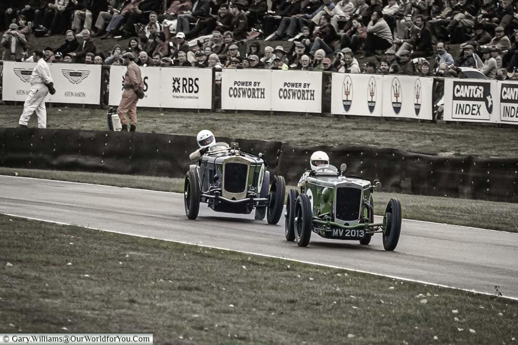 Two classic historic racing cars drifting as the blast around the madgwick corner on a grey overcast day at the goodwood revival meeting