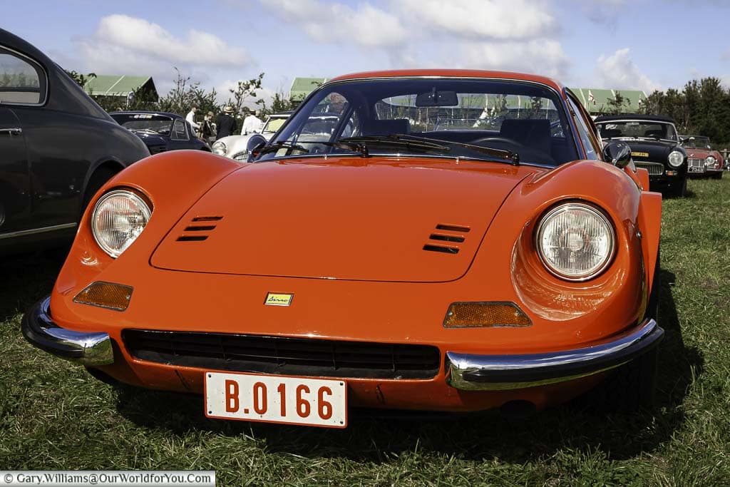 a close-up look at a bright red, late 1960's ferrari dino 206 gt in the car park of the goodwood revival