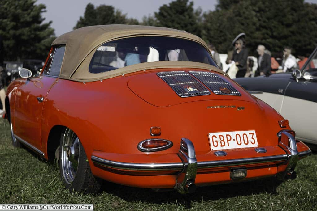 a close-up rear view of a bright red, 1961 porsche 356b super 90 soft top with a fawn-coloured roof in the car park of the goodwood revival