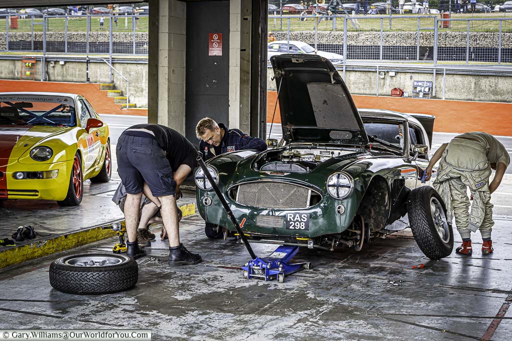 mechanics working on british racing green Austin Healey, raided on jacks, in the pits of brands hatch motor racing circuit in kent, england