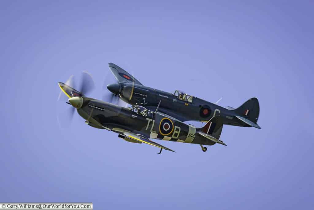 Two variants of world war two spitfires flying in close formation in the skies above the goodwood revival classic car race meeting