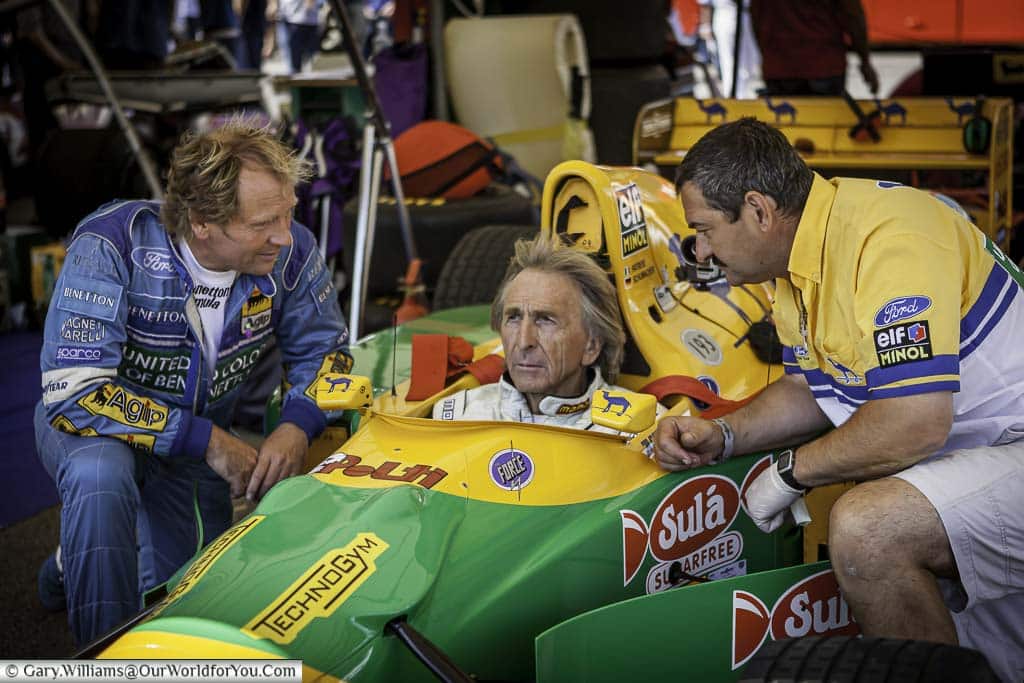 derek bell sitting in the cockpit of a 1980 benetton formula one racing car as he prepares to drive it up the hill at goodwood festival of speed