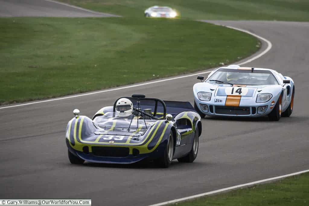 a mclaren-chevrolet m1m being chased down by a ford gt40 in the iconic gulf colours at the goodwood revival classic car race meeting