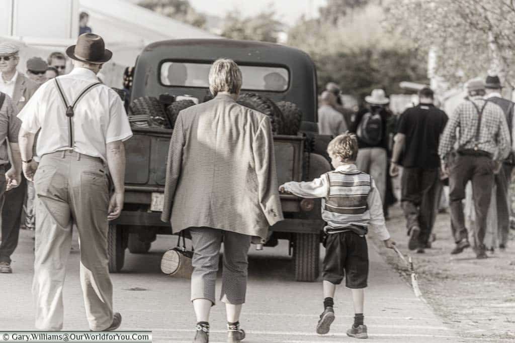 A family group dressed in period clothing from the 1940's following a historic pickup truck as they head away from the goodwood revival at the end of the day.