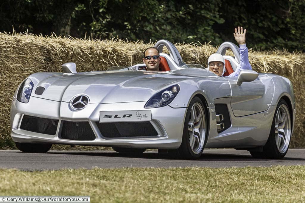The late sir stirling moss waving to the crowd as he drives a silver 2009 Mercedes slr stirling moss down the hill at goodwood festival of speed
