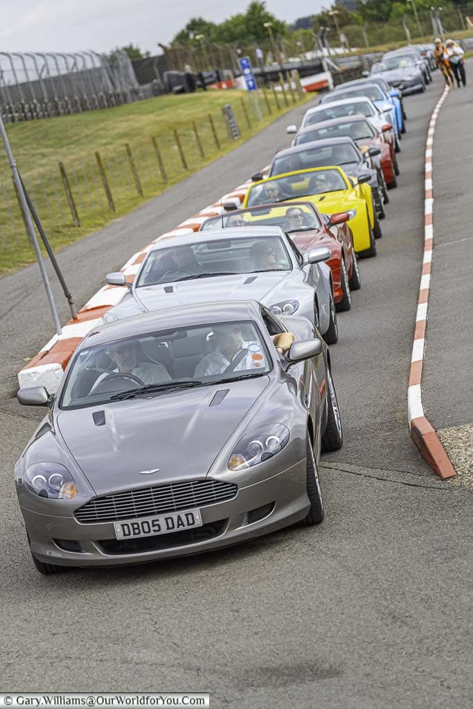 a stream of aston martins from the aston martin owners club - amoc, entering the pits of brands hatch motor racing circuit in kent, england