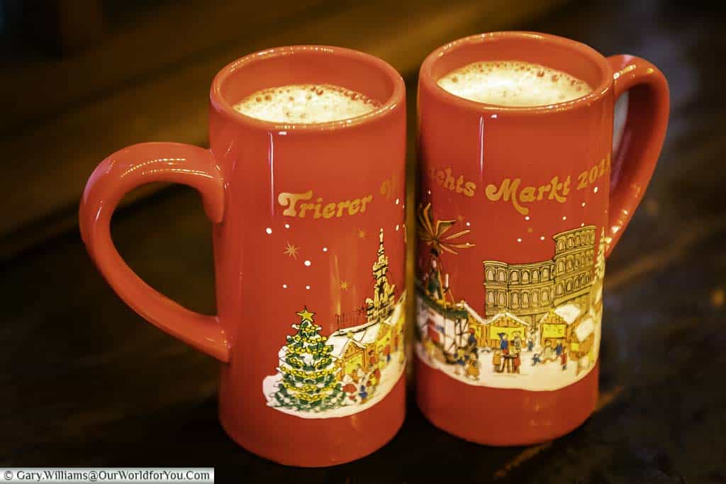 Two red christmas mugs of white glühwein on a wooden shelf in trier's german christmas markets