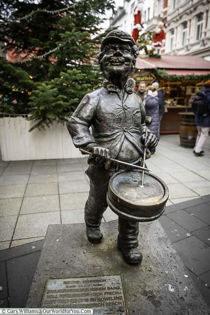 A comic bronze statues of resche hennerich playing a drum in front of the christmas market in münzplatz, koblenz