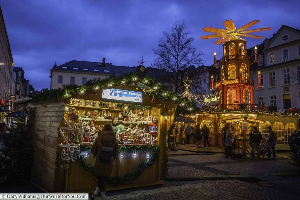 The entrance to am plan christmas market in koblenz at dusk, lined with stalls and the four-tier christmas pyramid taking centre stage.