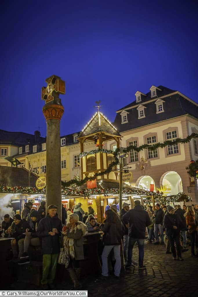 The illuminated historic marktkreuz mounted on a roman column in the centre of the trier hauptmarkt geman christmas market at dusk