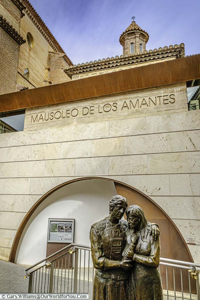A bronze statue of two lovers infront of the mausoleo de los amantes in teruel, spain