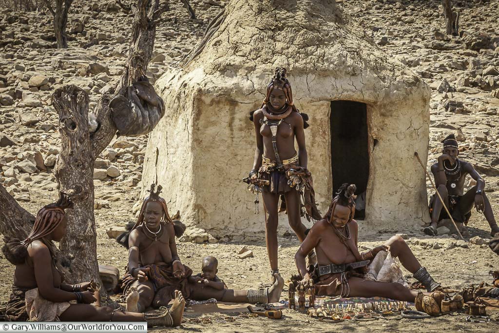 A group of the Himba people sitting with simple home gifts in front of them with a mud hut in the background