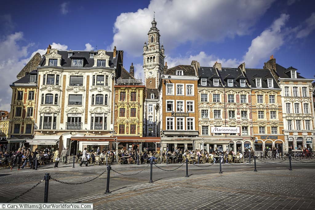 The scene of cafes that line the edges of Place Charles de Gaulle in Lille, northern France, underneath beautiful ornate buildings with the town's Clock tower in the background