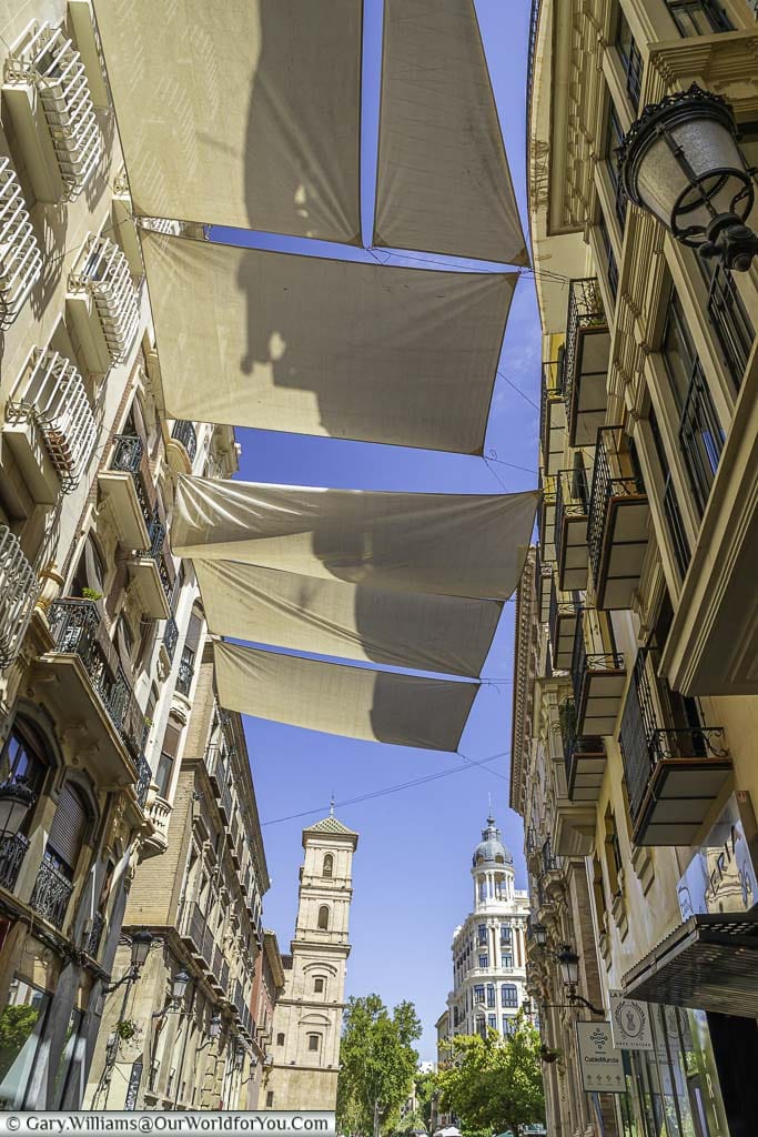 Sun screens over the calle trapería in murcia, with historic building in the distance