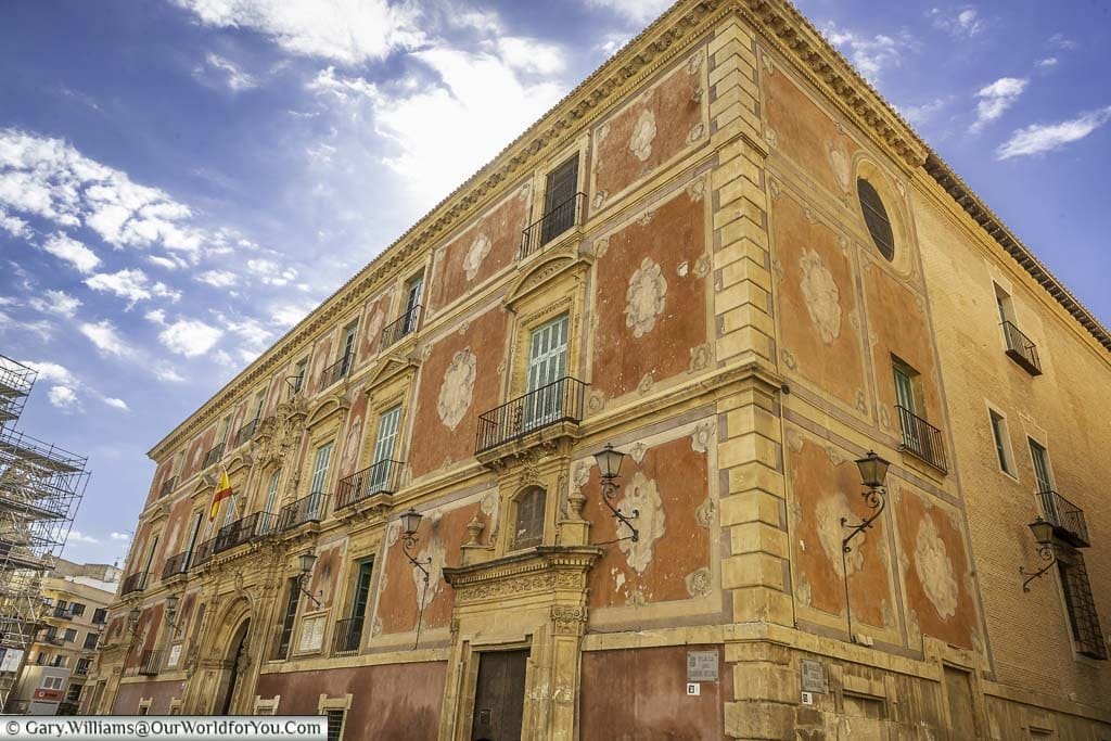 The exterior of the episcopal palace of murcia in ochre and sand colours, under a blue sky with scattered clouds