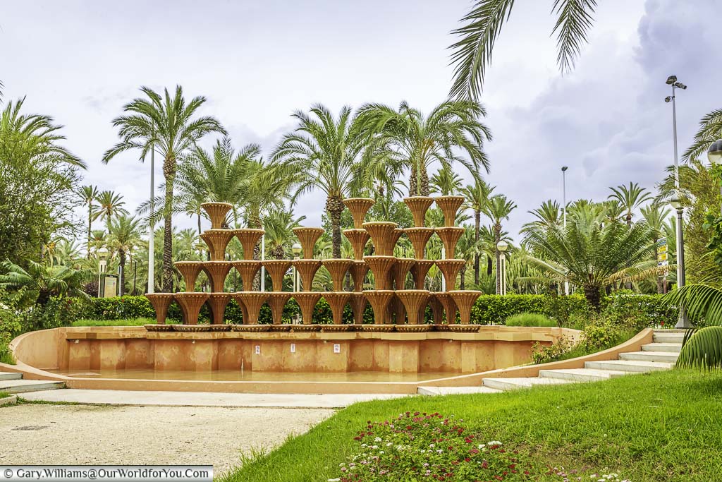 A photo of the modernist Fuente de la Glorieta fountain surrounded by palm trees. The fountain is located in Elche, Spain, which is known for its palm groves.