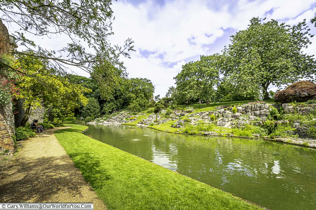 The moat around eltham palace as seen from the pathway alongside with the rockery and trees in the background.