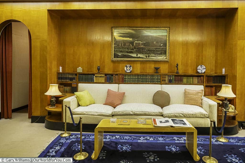 A sofa in the art deco boudoir in eltham palace in front of a bookshelf that runs a third of the height of the wood-panelled wall.
