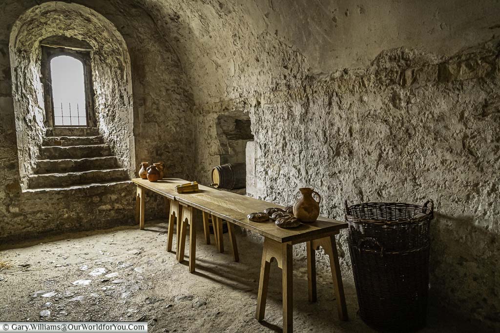 A basic stone toom with a single small window inside dover castle keep. A medieval wooden table is laid out with basic supplies and terracota jugs of ale
