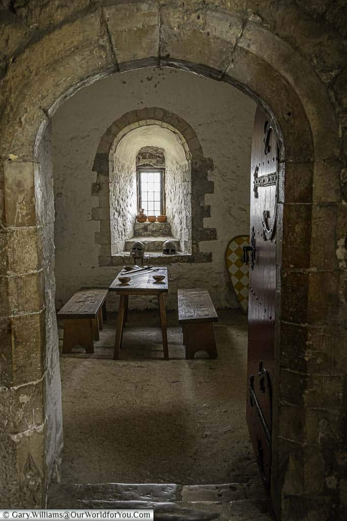 Looking through a medieval tone doorway to basic stone toom with a single small window inside dover castle keep. A medieval wooden table, flanked on either side with benches is laid out