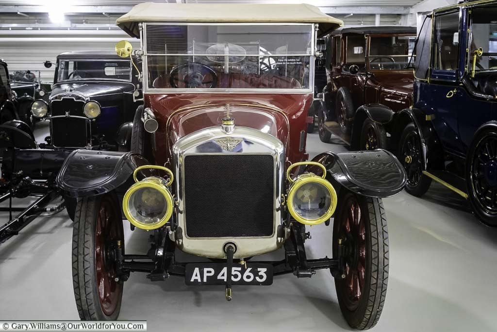 The frontal view of a 1914 Austin 20hp Vitesse Phaeton in a deep red colour in the Collections Centre of the British Motor Museum