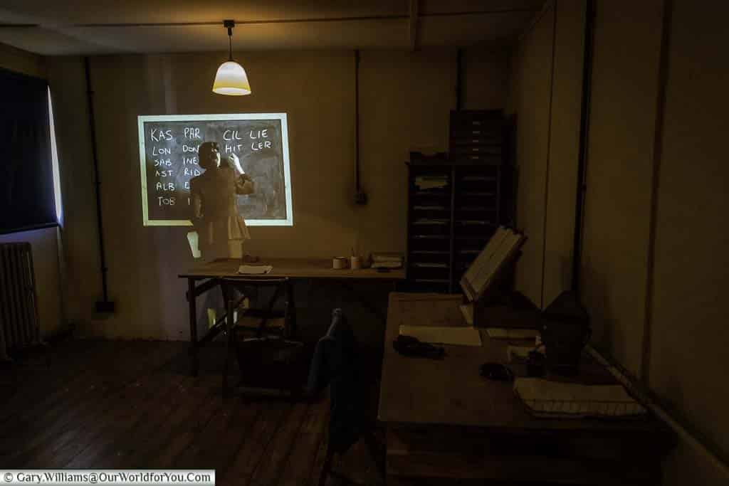 Inside a hut at Bletchley Park, with a holographic wartime codebreaker working on a code on a blackboard.