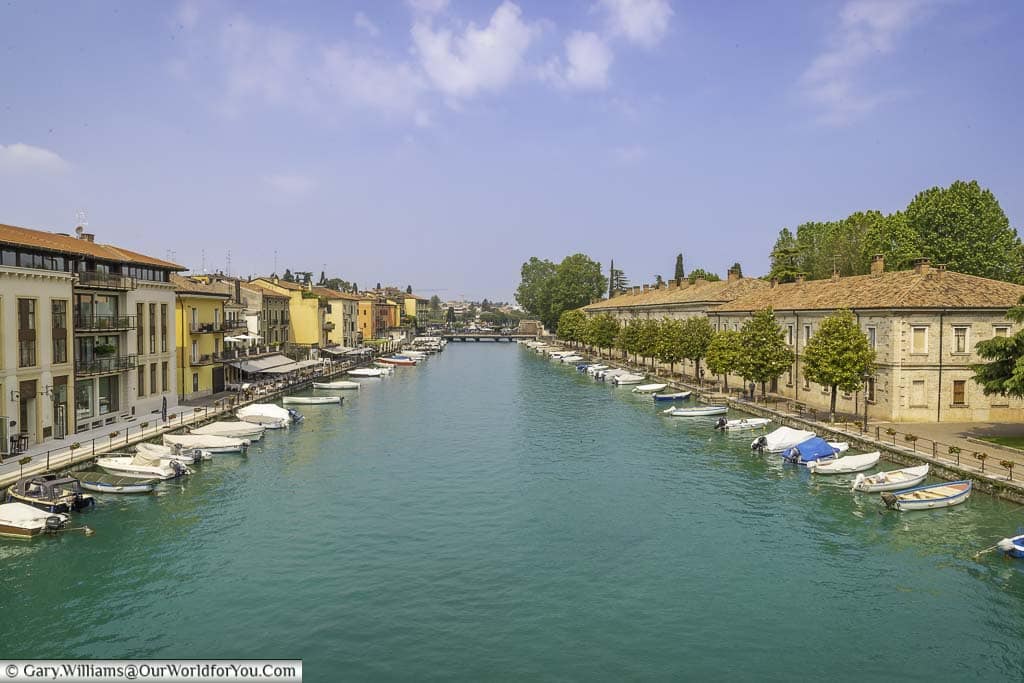 Overlooking a wide canal at Peschiera del Garda. It is linked directly to Lake Garda and on either side of the waterway are moored individual small boats with outboard motors.