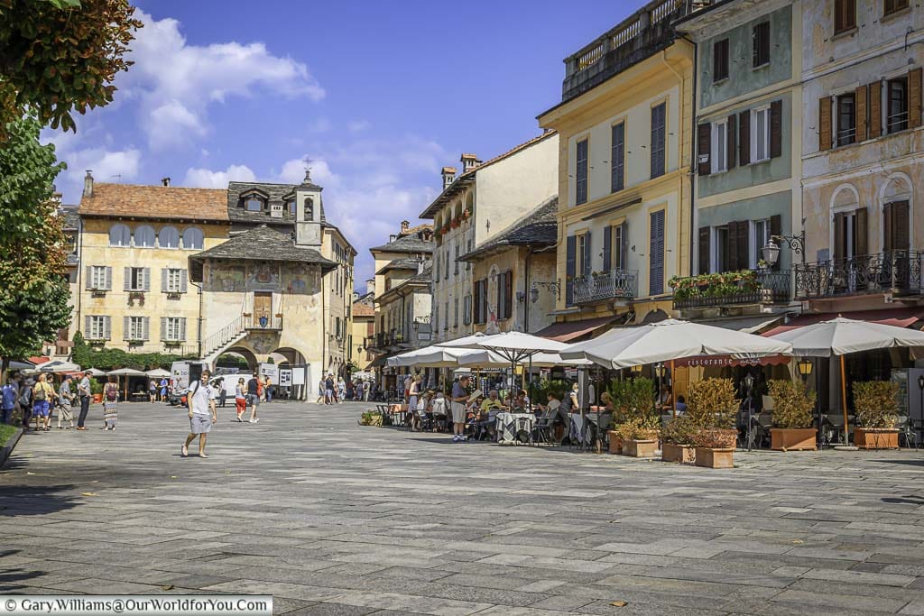 A historic square in Orta San Giulio, on the edge of Lake Orta, lined with restaurants with al fresco dining areas our front with their parasols keep the sun off the dinners.