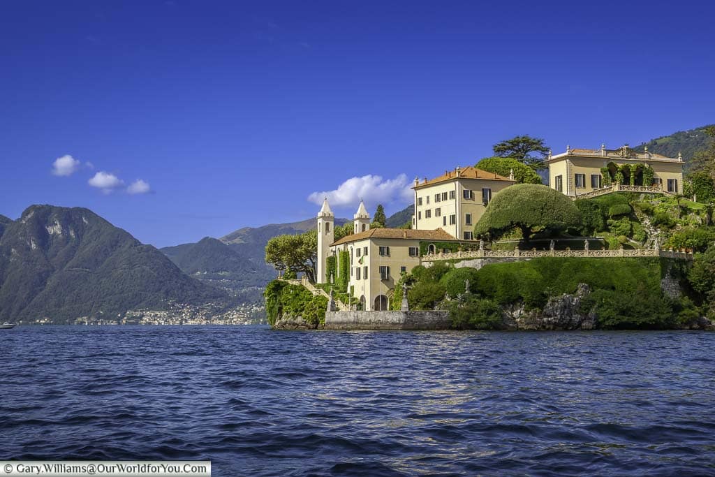 The palatial style Villa del Balbianello in sandy ones with terracotta tiled roofs against the backdrop of the deep blue water and blue skies of Lake Como
