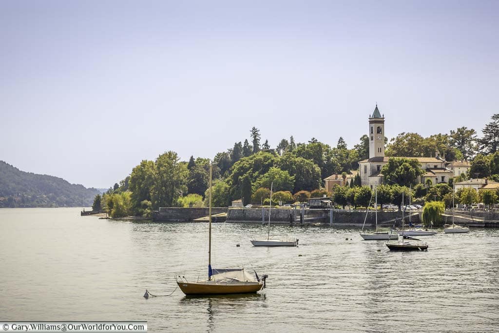 Sailing boats anchored on Lake Maggiore in front of a quiet town with its church tower clear on the shoreline.
