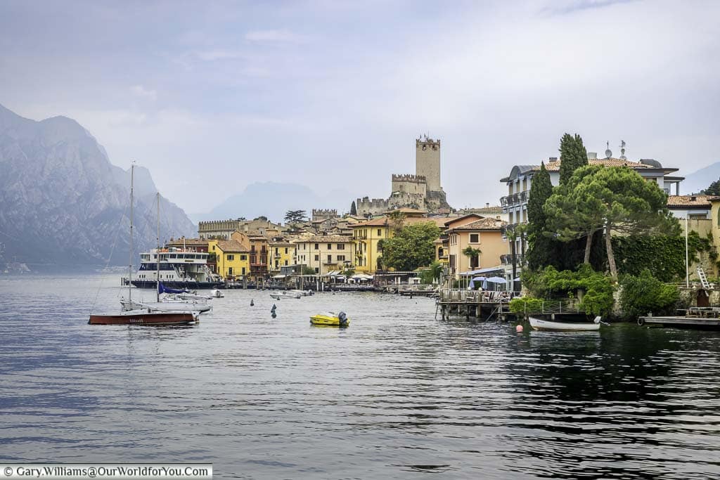 The pretty little lakeside town of Malcesine as seen from the water with boats bombing on the Lake and with its Castle dominating the skyline.