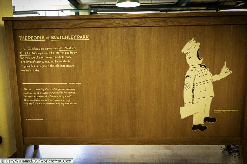 A wooden information board explaining that Bletchley Park's people came from all walks of life, civilian and military, with a cartoon character, from the era, of a loud military figure.