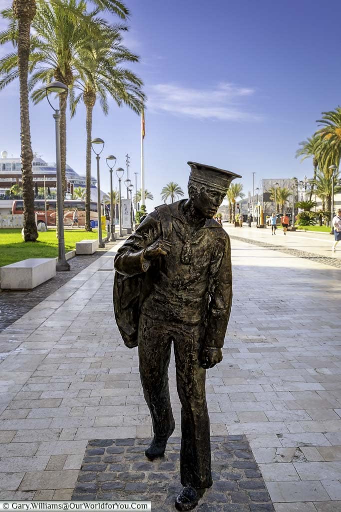 a bronze statue of a lone sailor, with his kit bag over his shoulder, walking the path from cartagena's harbour towards the town.