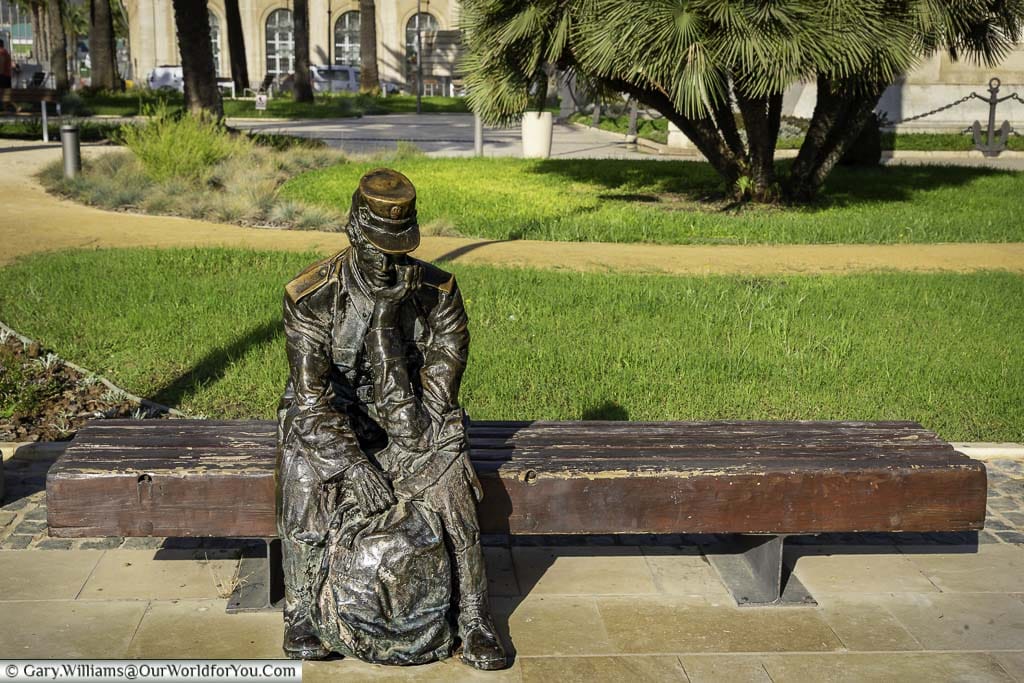 a bronze statue of a seated 18th century solder on a wooden bench in cartegena in southern spain